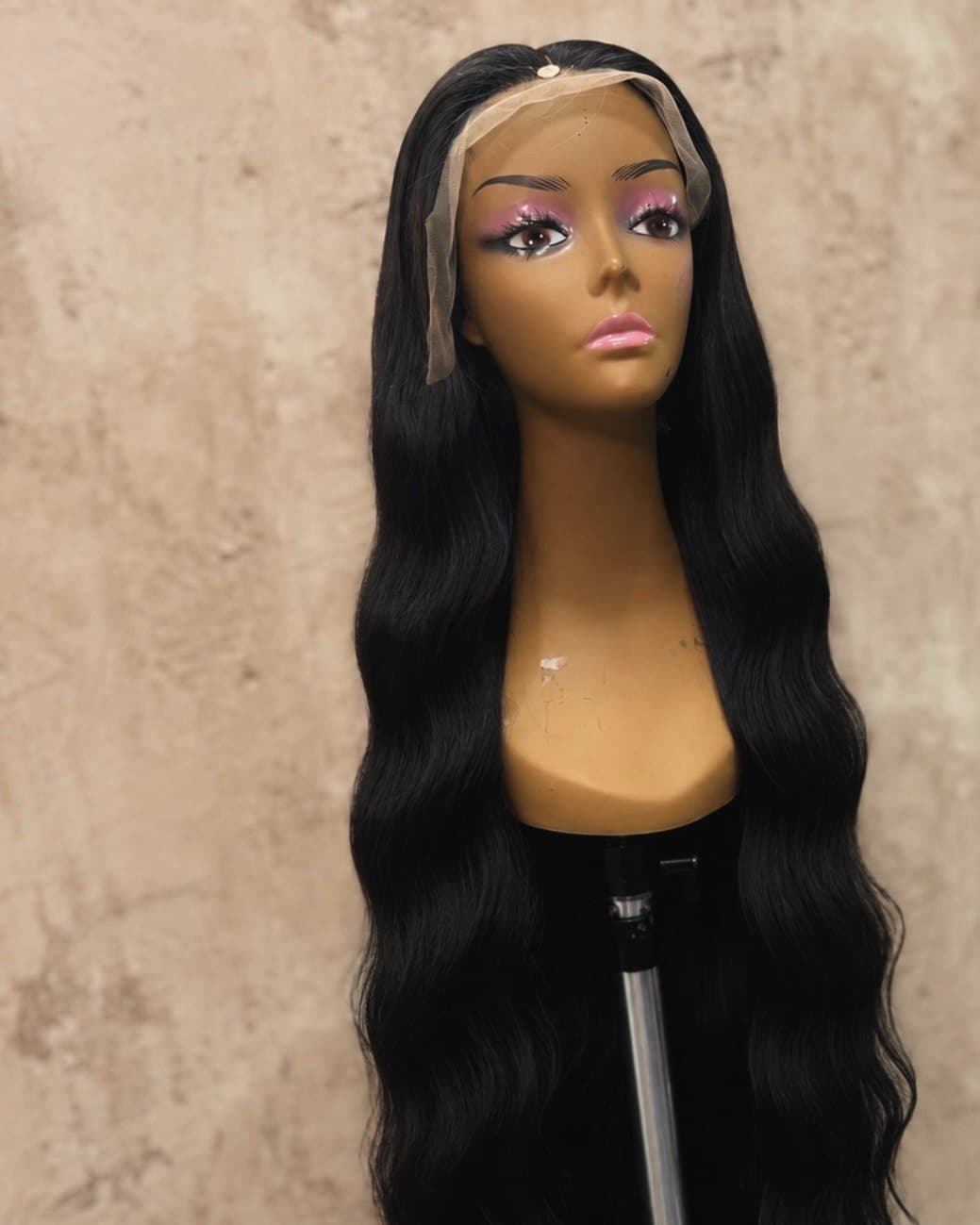 A long black body-wave unit on a stand, falling well past the shoulders of the block.